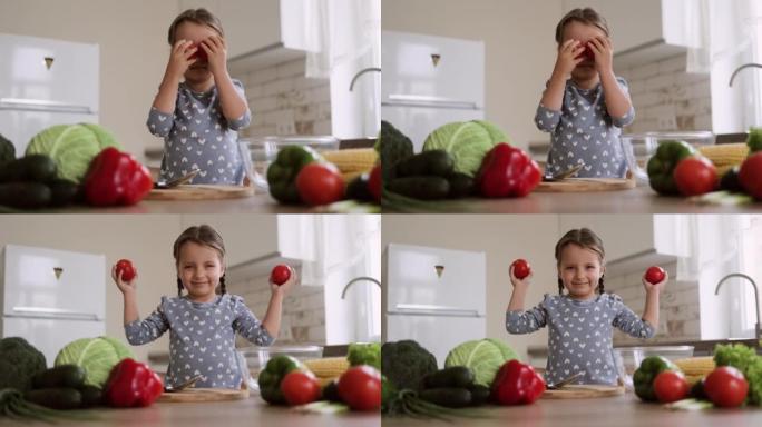 微笑的女孩穿着便服玩耍，用西红柿闭上眼睛，对烹饪沙拉感到满意