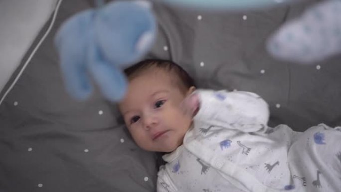 一个新生婴儿躺在婴儿床里，看着玩具手机。摇篮里的孩子。