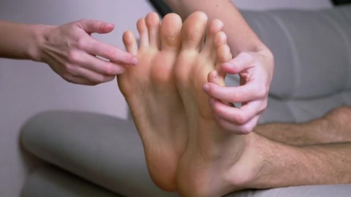女人的手挠男人的光脚，脚趾，在沙发上伸展。近距离