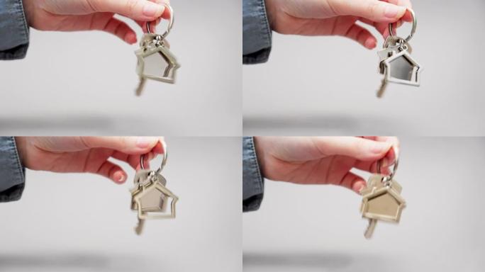 女人的衬衫特写镜头用金属钥匙扣屋摇动新钥匙。灰色背景。抵押、租赁和房地产的概念