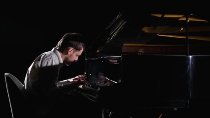 男人在黑色背景上弹钢琴。音乐家钢琴家在黑暗中表演，同时在音乐键盘乐器上表演经典爵士音乐会。特写。以5