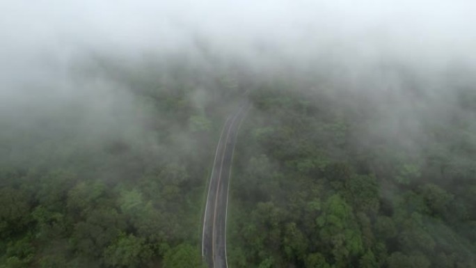 空中无人机电影拍摄的汽车和道路在早上下雨后越过山顶，有雾和绿色森林。