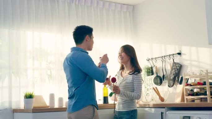 亚洲年轻夫妇在情人节碰杯酒。可爱的浪漫新婚姻男女在家里的厨房里一起举行晚宴庆祝结婚周年纪念日