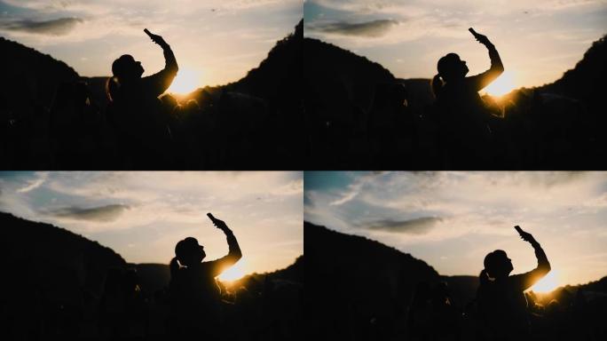 一个女孩和其他人的轮廓，映衬着山里美丽的日落。女孩用手机拍照