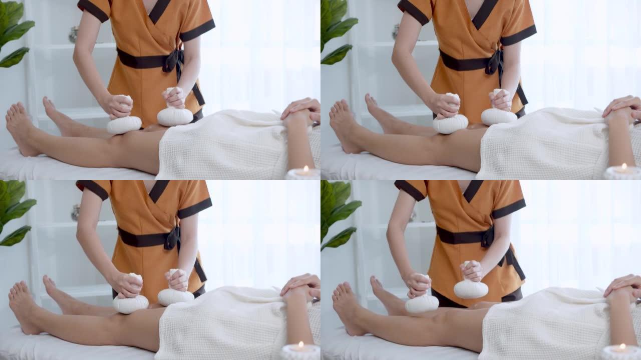 按摩师在水疗按摩室用热敷对女性进行腿部按摩。女人因身体疼痛而接受按摩治疗。