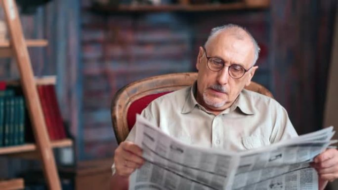 专注的老人阅读纸质报纸文本在乡村家庭室内的扶手椅上放松
