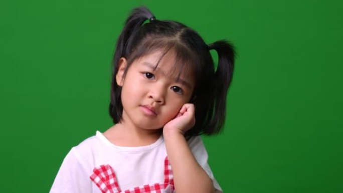 快乐的亚洲儿童女孩的肖像运动到绿屏背景上的相机，一个孩子看着相机。学龄前儿童做梦充满能量感觉健康和良