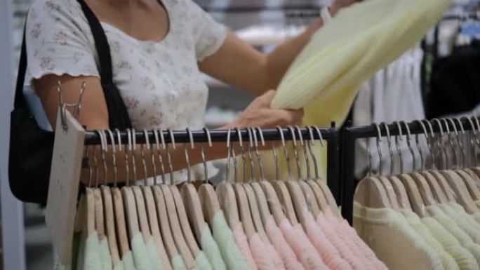 服装店的顾客选择柔和的彩色开衫，从商场的大众市场商店购买时尚服装。不同尺寸和型号的连衣裙挂在衣架上出