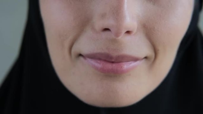 一个穿着黑色头巾的女人的嘴唇特写，一个穆斯林女人美丽的微笑。伊斯兰世界的善良与和平概念。女人嘴的特写