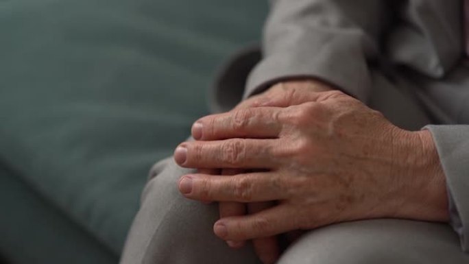 一个面目全非的老妇的手的特写。成熟的女人双手交叉在皱纹和膝盖上的老年斑。老年