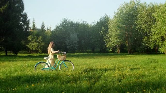 夏季，骑自行车的女人在乡村道路上骑自行车。穿着衣服的美女骑自行车的人在地面小径上骑自行车，绿色的草地