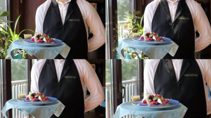服务员沿着全景窗户向客户端着一盘美味的沙拉。一位穿着白衬衫和黑色围裙的服务员在一家现代餐厅用餐