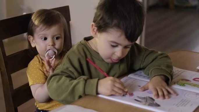 男孩画画和小妹妹坐在同一把椅子上，哥哥照顾他的妹妹。儿童发展。彩色肖像。婴儿发育。
