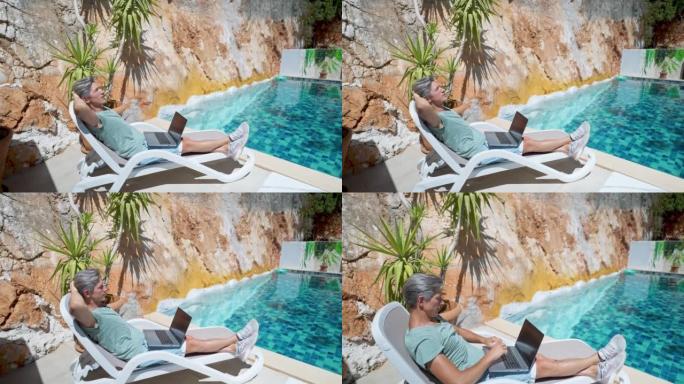 在度假酒店度假期间，放松成年男子在游泳池边放松，在笔记本电脑空屏幕上观看新闻或视频