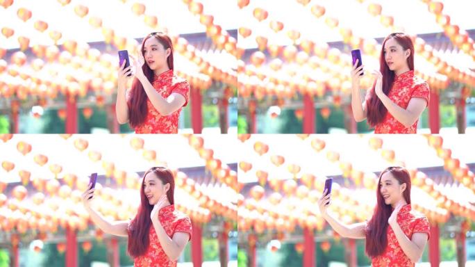 快乐的亚洲女性穿着红色的中国传统旗袍，旗袍装饰，与情人视频通话，手持智能手机，对着前置相机自拍
