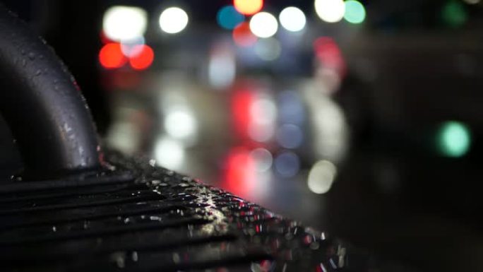 公共汽车站长椅上的汽车交通灯反射。水雨滴在湿金属上。
