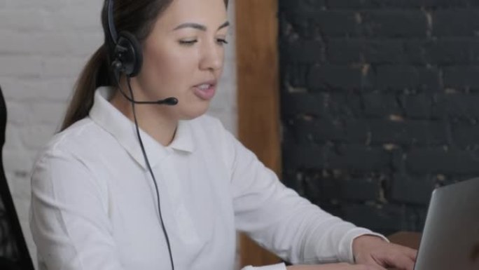 微笑的女性呼叫中心接线员，客户支持代理戴着耳机咨询客户在笔记本电脑上的在线打字，在互联网上聊天，帮助