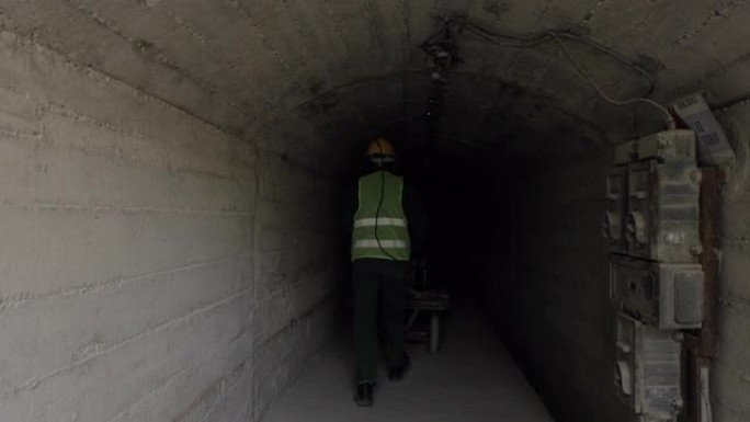 戴着头盔和设备的矿工从后面推小车，穿过矿井隧道。