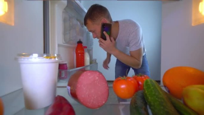 男子在手机通话，打开冰箱门，取出牛奶