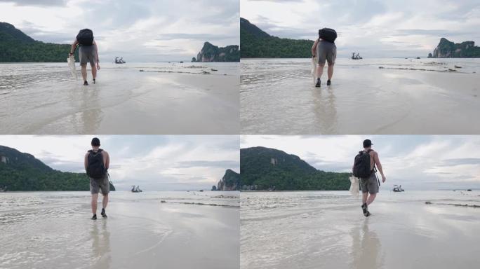 亚洲男性背包旅游志愿者手持塑料垃圾袋走进低潮海水，积极的自然环境和人，垃圾清除活动，可持续旅游