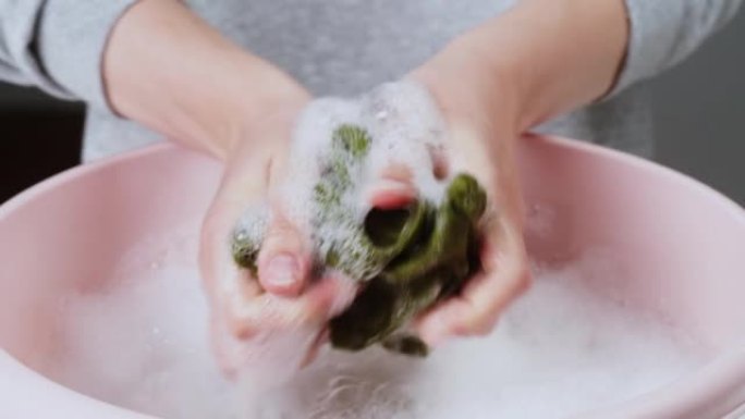 用泡沫和洗衣粉特写在盆中拧干绿色毛巾，用洗涤剂处理变质的脏衣服。洗衣、洗手的概念。去污剂广告