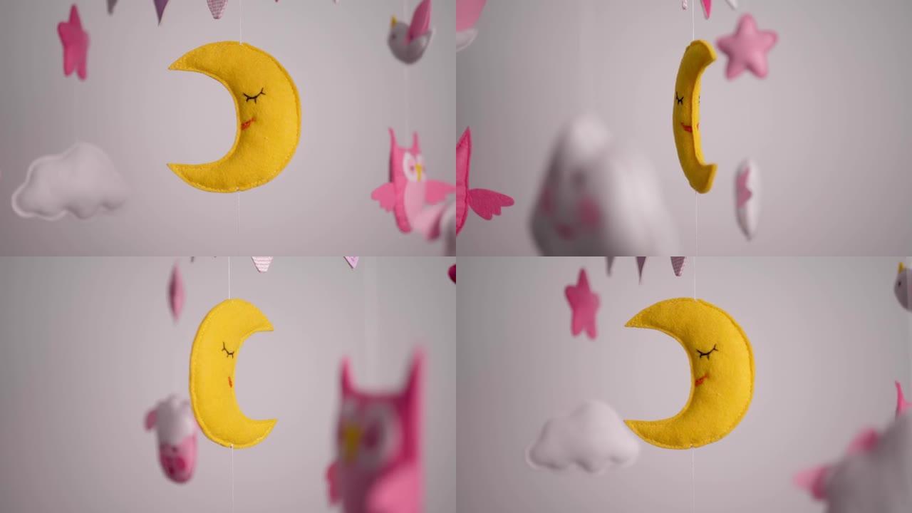 婴儿手机，带有粉红色手工缝制的动物和鸟类玩具，白色墙壁背景上有黄色的月亮。