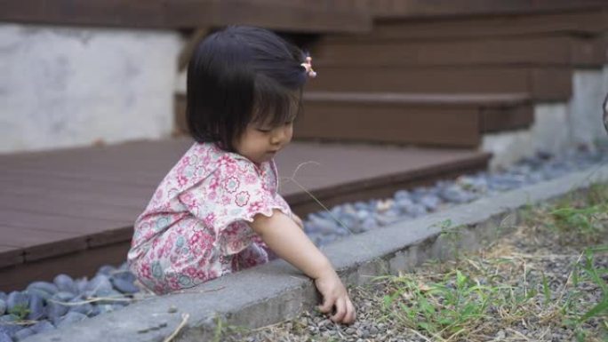 在阳光明媚的日子里，穿着和服的无辜亚洲女性蹒跚学步的孩子在她传统的日本房子外面的花园里独自玩弄泥土。