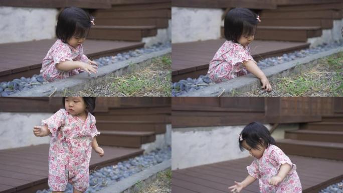 在阳光明媚的日子里，穿着和服的无辜亚洲女性蹒跚学步的孩子在她传统的日本房子外面的花园里独自玩弄泥土。