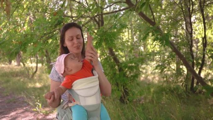 夏天的公园里，妈妈带着刚出生的宝宝在吊带上散步，探索周围的世界