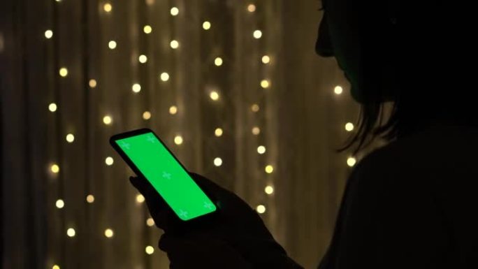 女人拿着色度键绿屏智能手机。浏览互联网，观看内容的样机