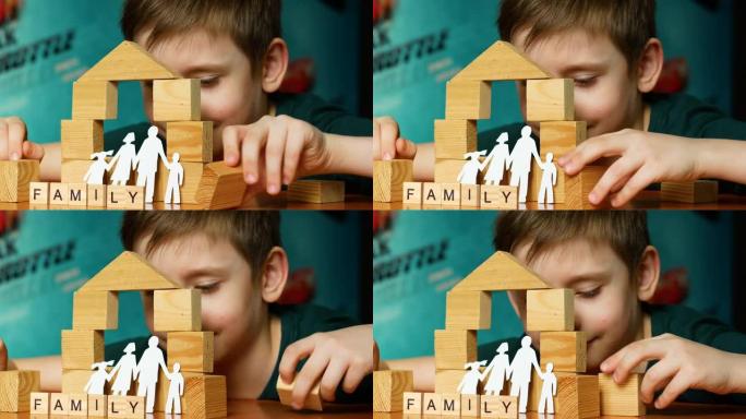 一个7岁的高加索男孩用木制立方体建造了一个玩具屋，即铭文家族，一个家庭的剪影是用纸剪掉的。孩子的梦想