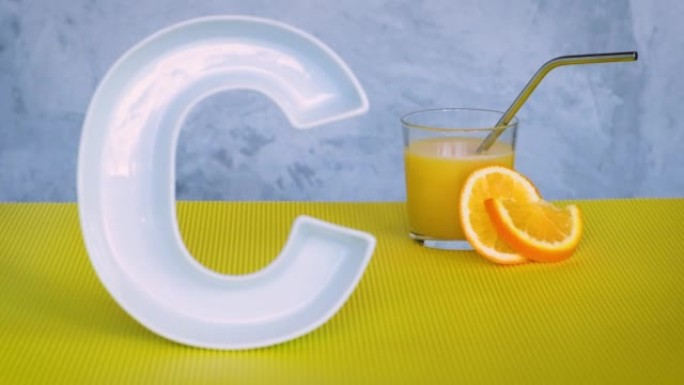食品中的维生素c，营养保健品概念。将焦点从大陶瓷字母C转移到带有鲜榨橙汁的玻璃上，然后返回。抗坏血酸