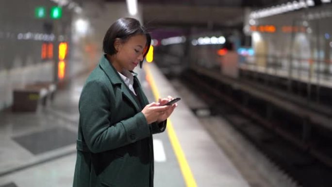 带着智能手机在地铁站台上微笑的非洲裔妇女，在地铁中使用无线互联网的黑人女性