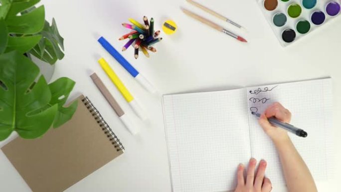 这孩子正在学习写作。孩子们用黑色的毡尖笔在学龄前儿童的桌子上画着笔记本。孩子为学校写台词。孩子们的手