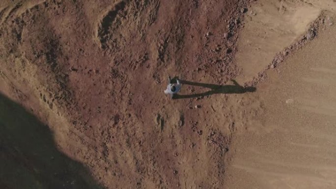 从上方看俯视图。穿着原始服装的年轻人站在沙漠或另一个星球上的废弃土地上行走。男孩在荒地迷路了。慢动作