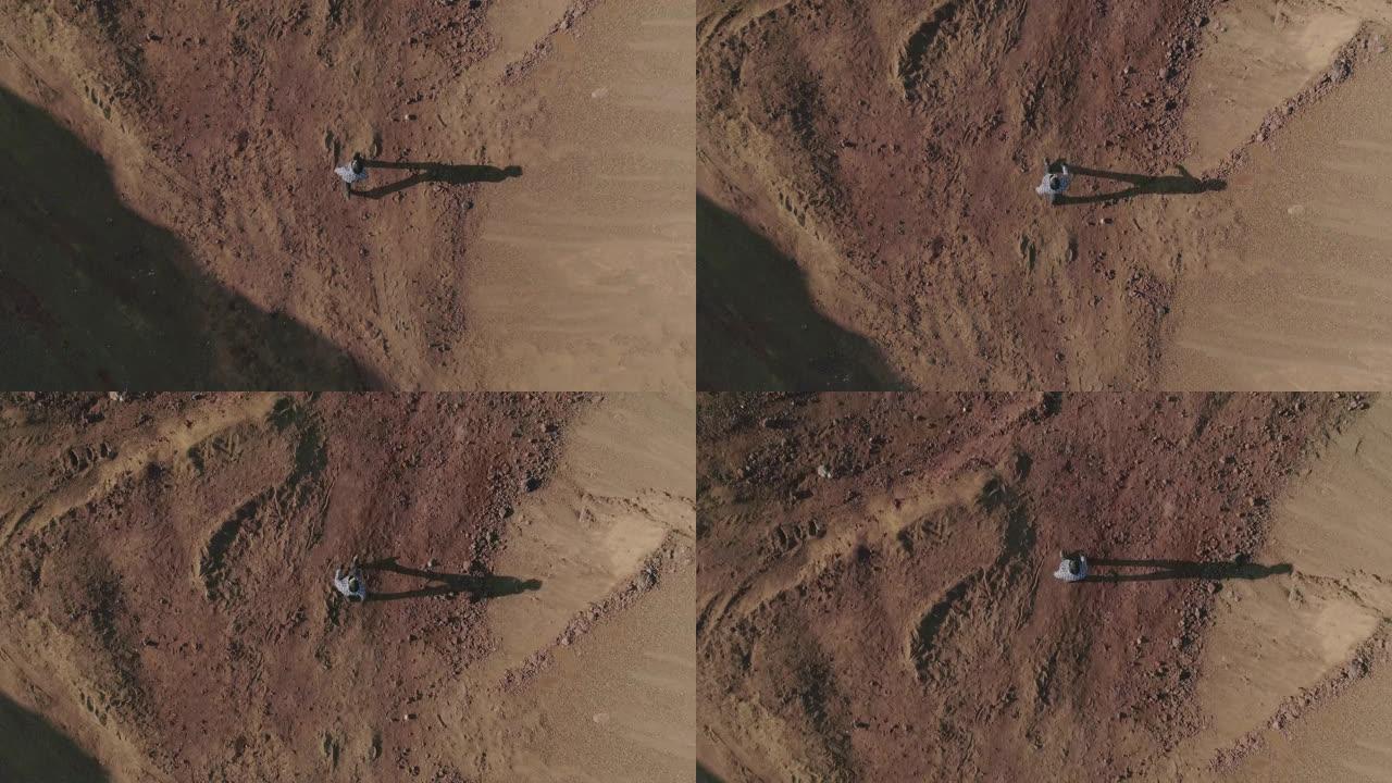 从上方看俯视图。穿着原始服装的年轻人站在沙漠或另一个星球上的废弃土地上行走。男孩在荒地迷路了。慢动作
