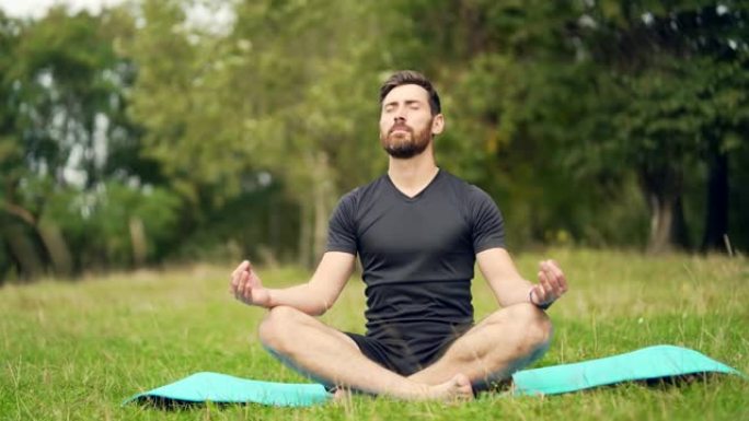 健康英俊的高加索大胡子男人在公园冥想，坐莲花姿势练习瑜伽垫，禅