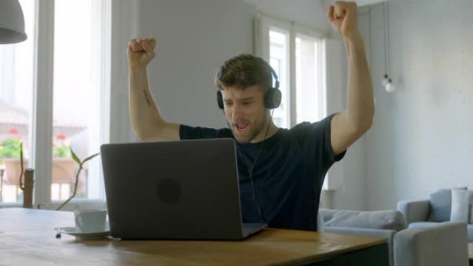 在笔记本电脑屏幕上阅读好消息时，举手庆祝胜利的人