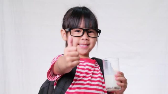 可爱的女学生上学前喝玻璃杯里的牛奶。儿童健康营养。回到学校的概念