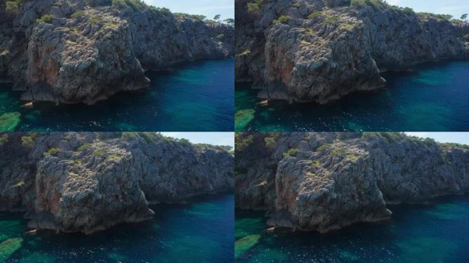 无人机在伊比沙岛的岩石悬崖海岸线和蓝色海洋周围飞行