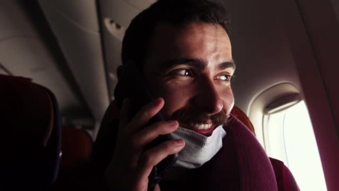 年轻的白人男子坐在飞机内，手里拿着智能手机聊天