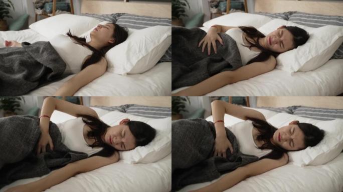 亚洲女孩醒来时肚子疼，睡在床上，早上在家里的一个现代床室里，肚子不舒服。