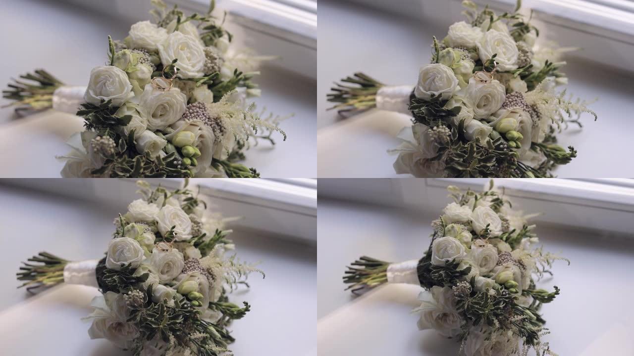 婚礼金戒指躺在白色窗台上美丽的婚礼白玫瑰花束上