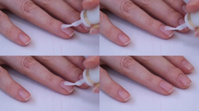 女人的手靠近。这个女孩用透明的医用清漆覆盖指甲。天然美甲。指甲护理。在治疗剂的帮助下加强指甲
