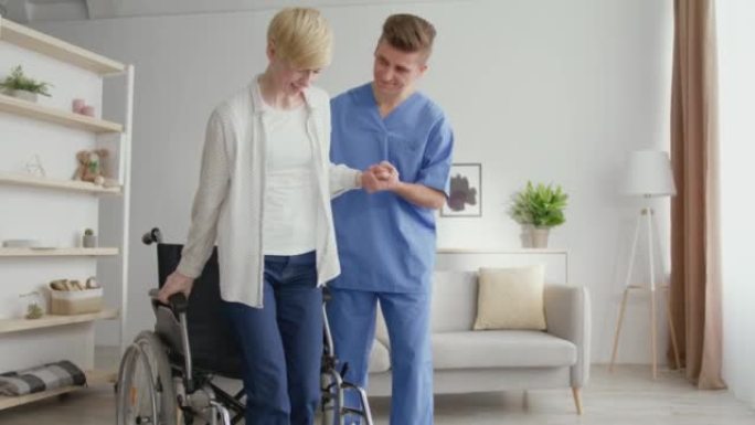 专业的男性治疗师帮助成熟的女性从轮椅上站起来走路，在事故发生后变得健康