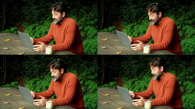 成年男子微笑着，坐在自然公园和树林中与笔记本电脑一起进行在线电话会议。现代工作的概念无处不在和另类办