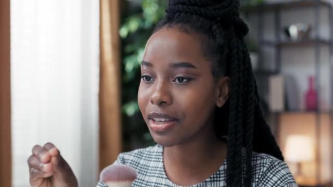 化妆师在非裔美国血统的黑皮肤女人脸上的环灯后面的特写镜头中，与她提供美容建议的粉丝交谈，描述了她使用