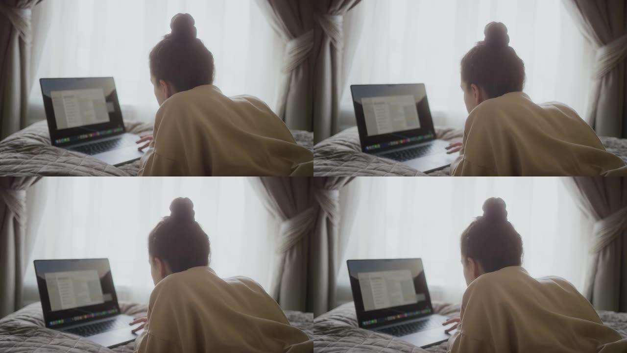 集中的女人在笔记本电脑上工作。女性自由职业者使用现代PC。女士拿着笔记本躺在床上。女性博客作者家庭工