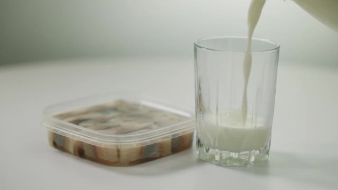 罐装鲱鱼放在桌子上，白色牛奶倒入玻璃中。特写室内不相容的食物和饮料。