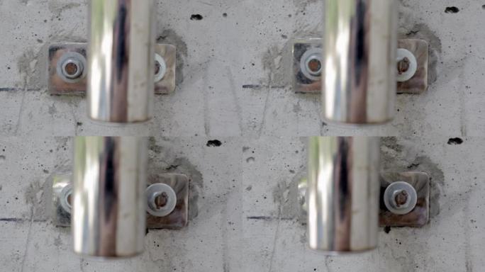 螺栓在混凝土墙宏观特写素材。用螺栓将镀铬的栏杆管紧固到混凝土墙上。螺栓拧入其他螺栓旁边的混凝土中。灰